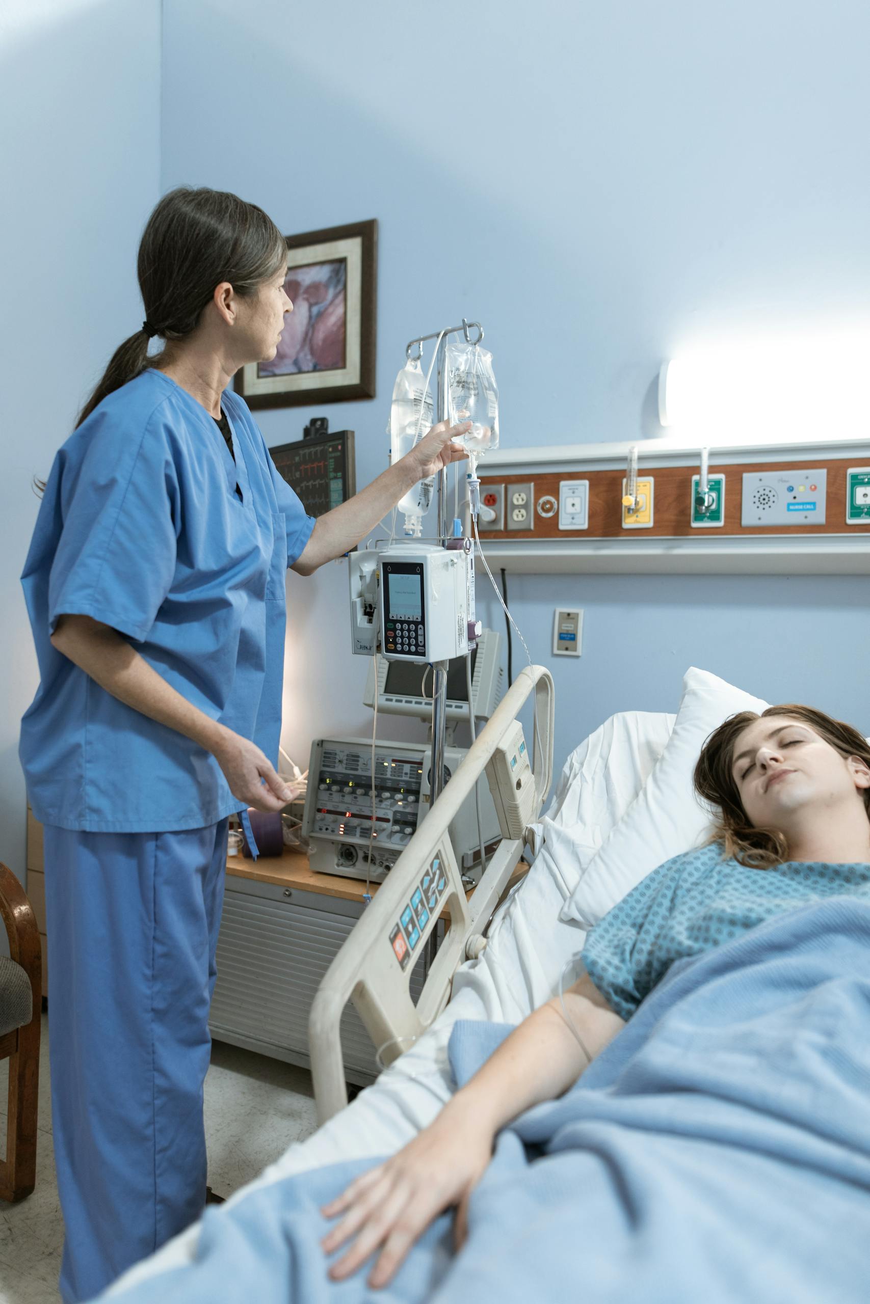 a nurse attends to a patient in a hospital room ensuring medical equipment is functioning. 6129677 scaled