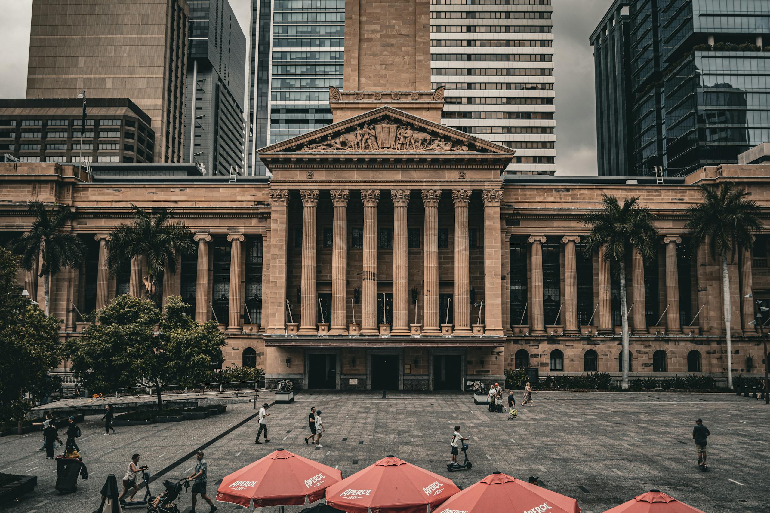 a view of brisbane city hall with urban surroundings and pedestrians in the plaza. 29339607 scaled