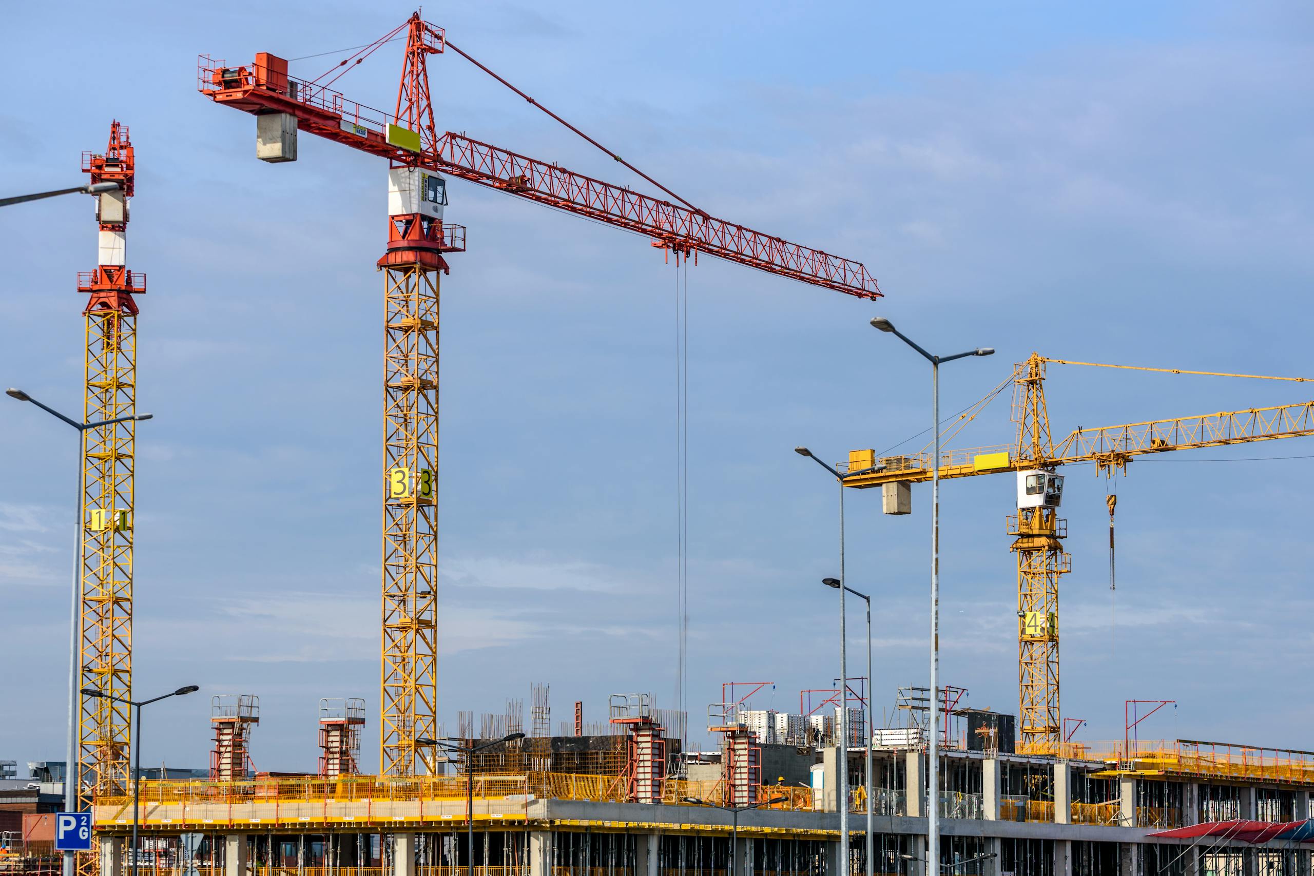 multiple tower cranes working on a large construction site with blue sky backdrop. 224924 scaled