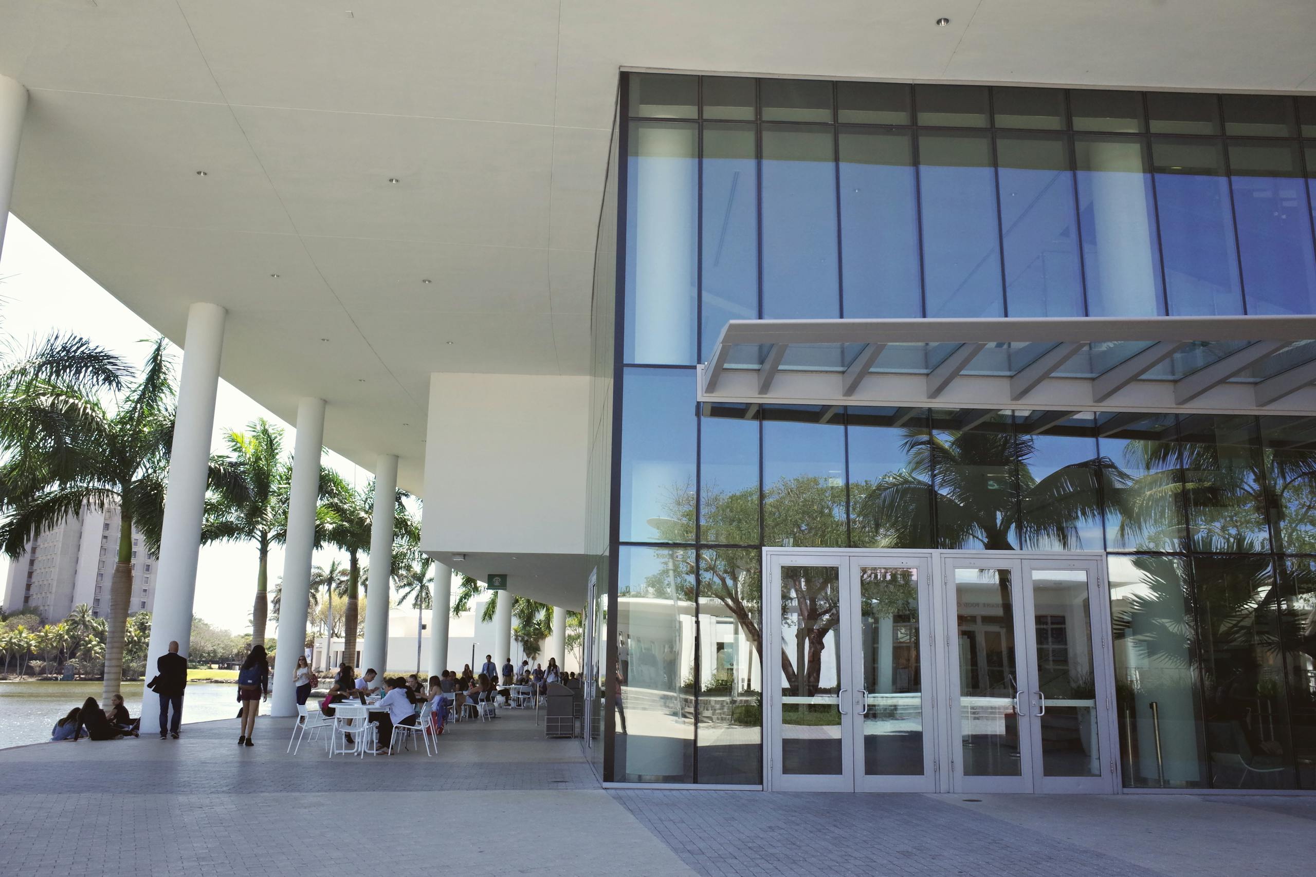 students socialize under a modern building on a sunny university campus. 31085764 scaled