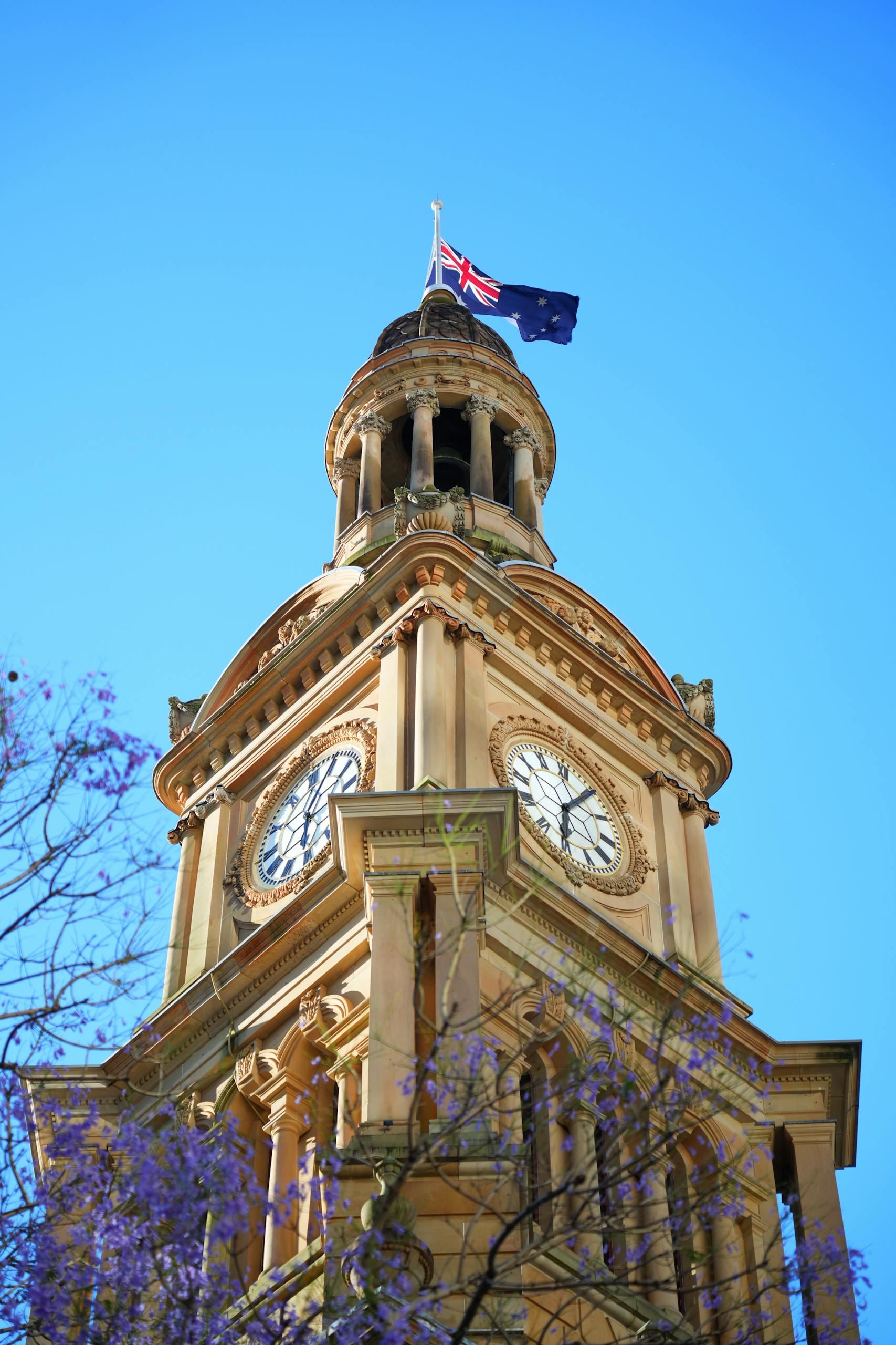 view of sydney town halls clock tower and australian flag against a clear blue sky. 34736682 scaled